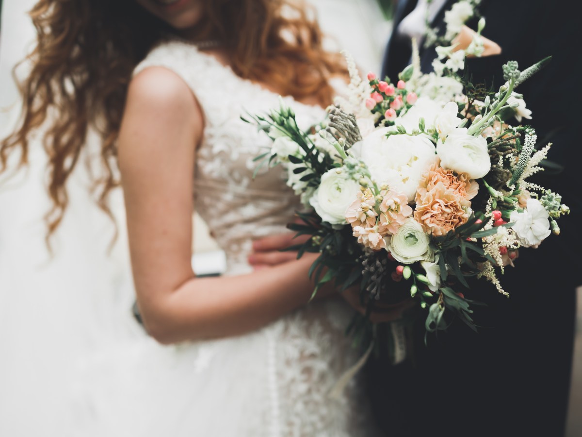Bride in white dress holding floral bouquet with pastel flowers.