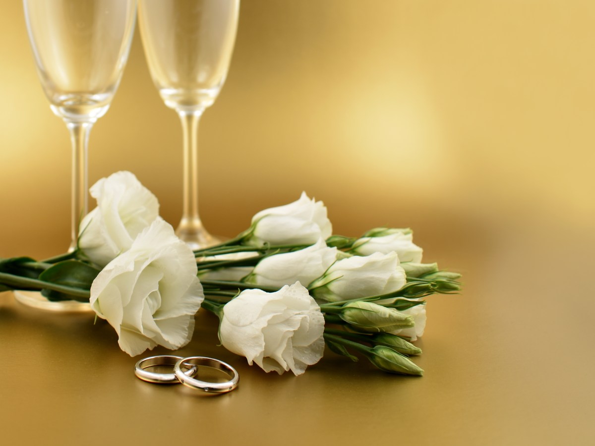 Two champagne flutes, white roses, and wedding rings on a gold background.