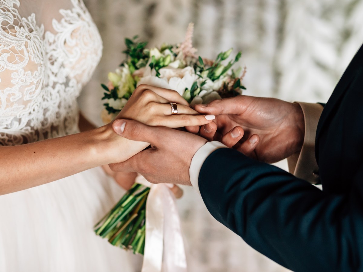 Couple holding hands, woman in bridal gown with bouquet, ring exchange visible.