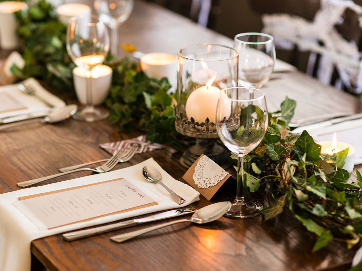 Elegant table setting with candles, greenery, and glassware on a wooden surface.