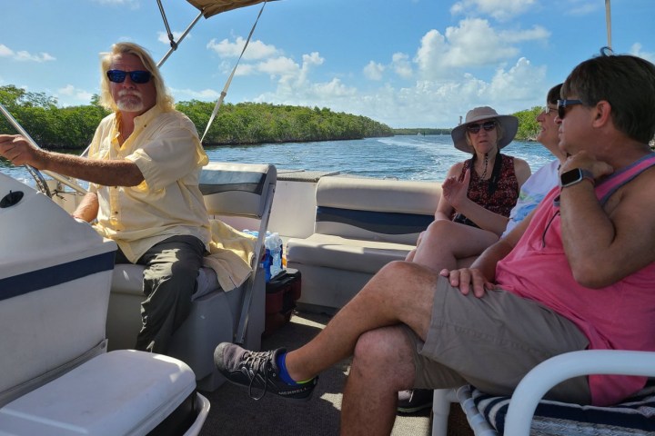 Four people relaxing on a boat under a canopy, cruising on a sunny day.