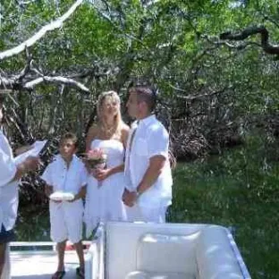 Outdoor wedding ceremony on a boat in a mangrove with people in white clothing.